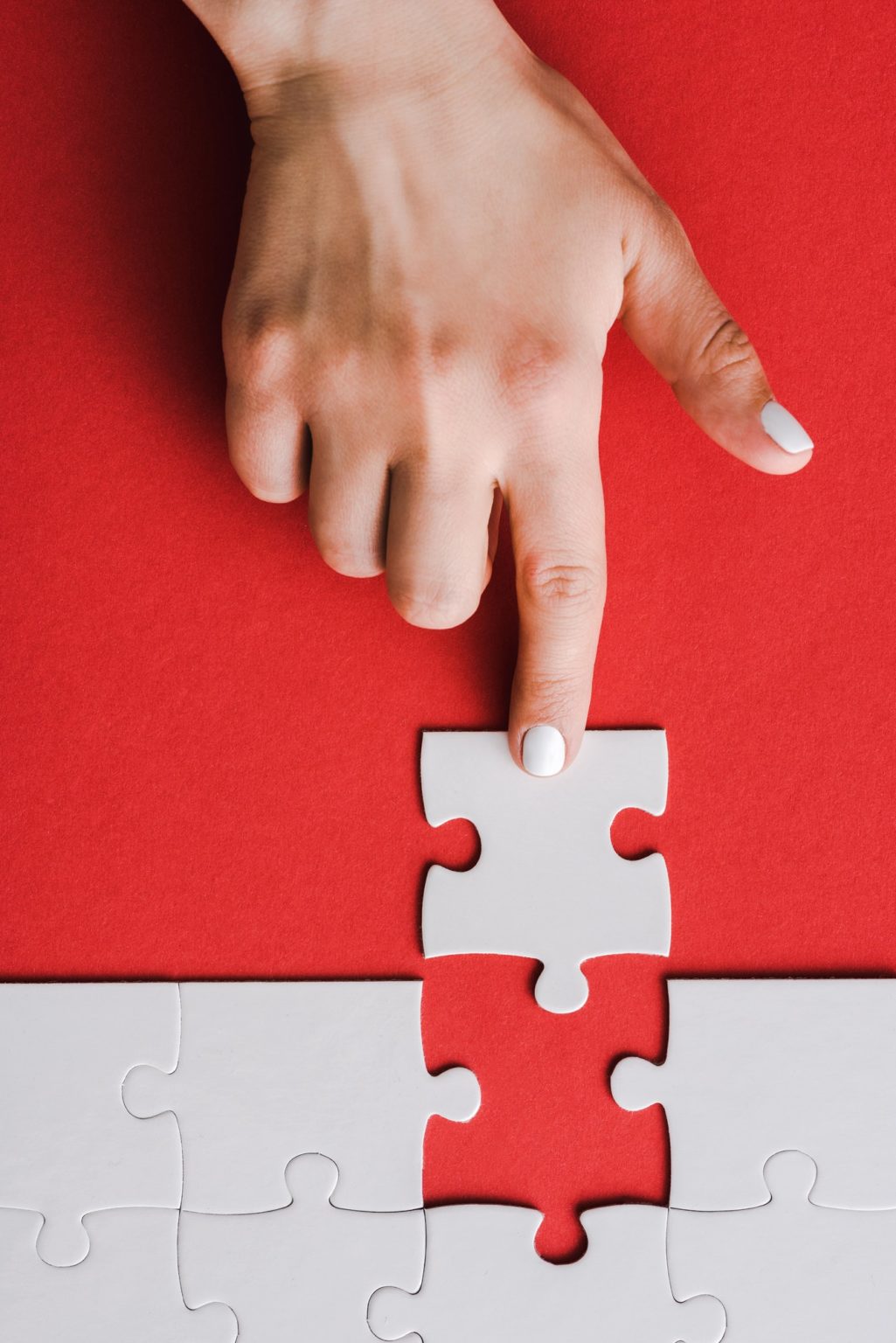 top view of woman pointing with finger at jigsaw near connected white puzzle pieces on red